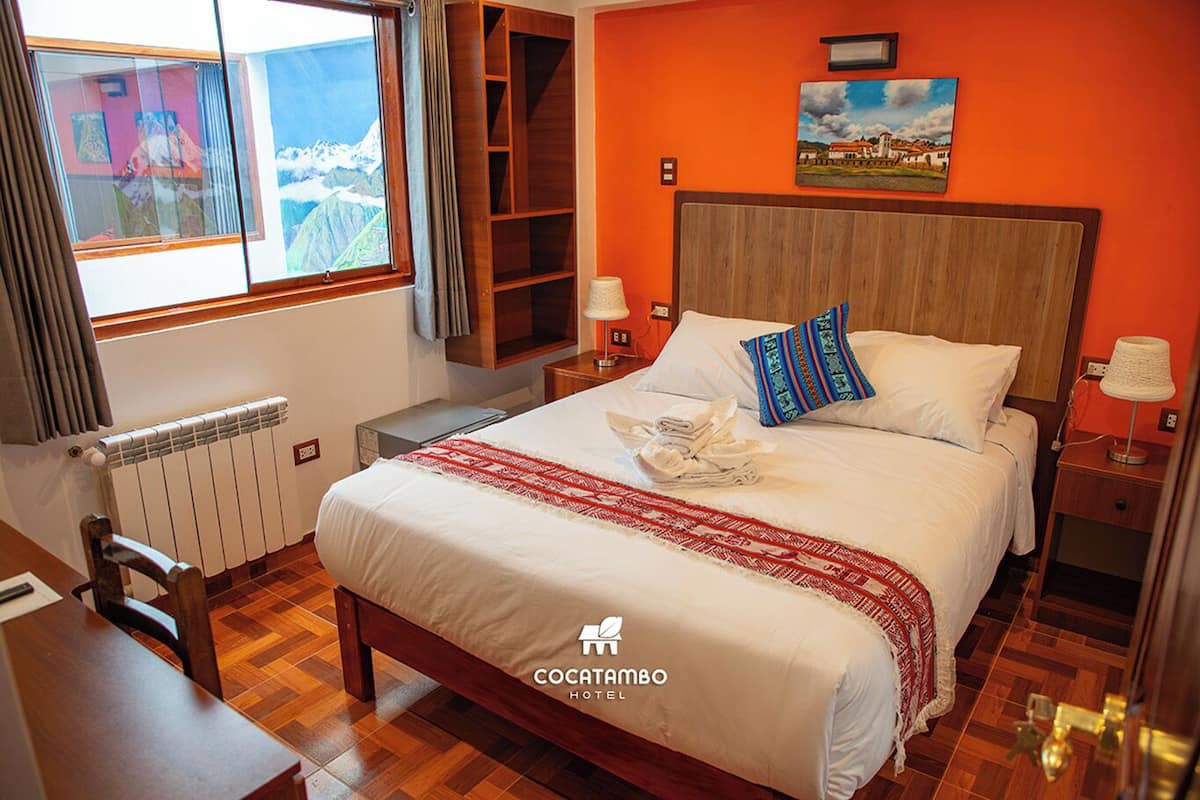 A hotel room with a wooden bed, a view of mountains through a window, a radiator, and a wooden floor.
