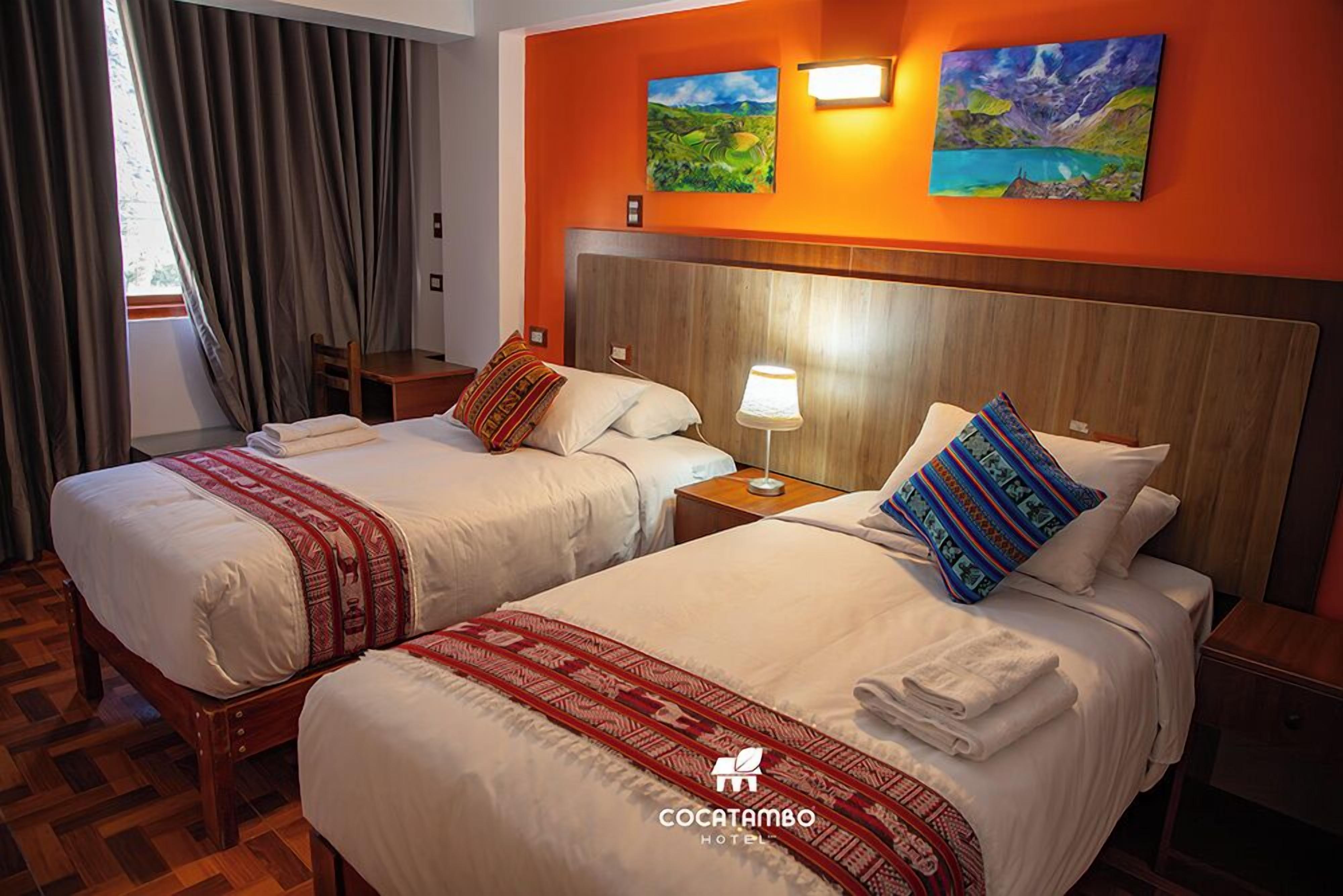 Ein Hotelzimmer mit zwei Betten, einem Holz-Kopfteil, einem Nachttisch mit Lampe und einem Bild an der Wand.