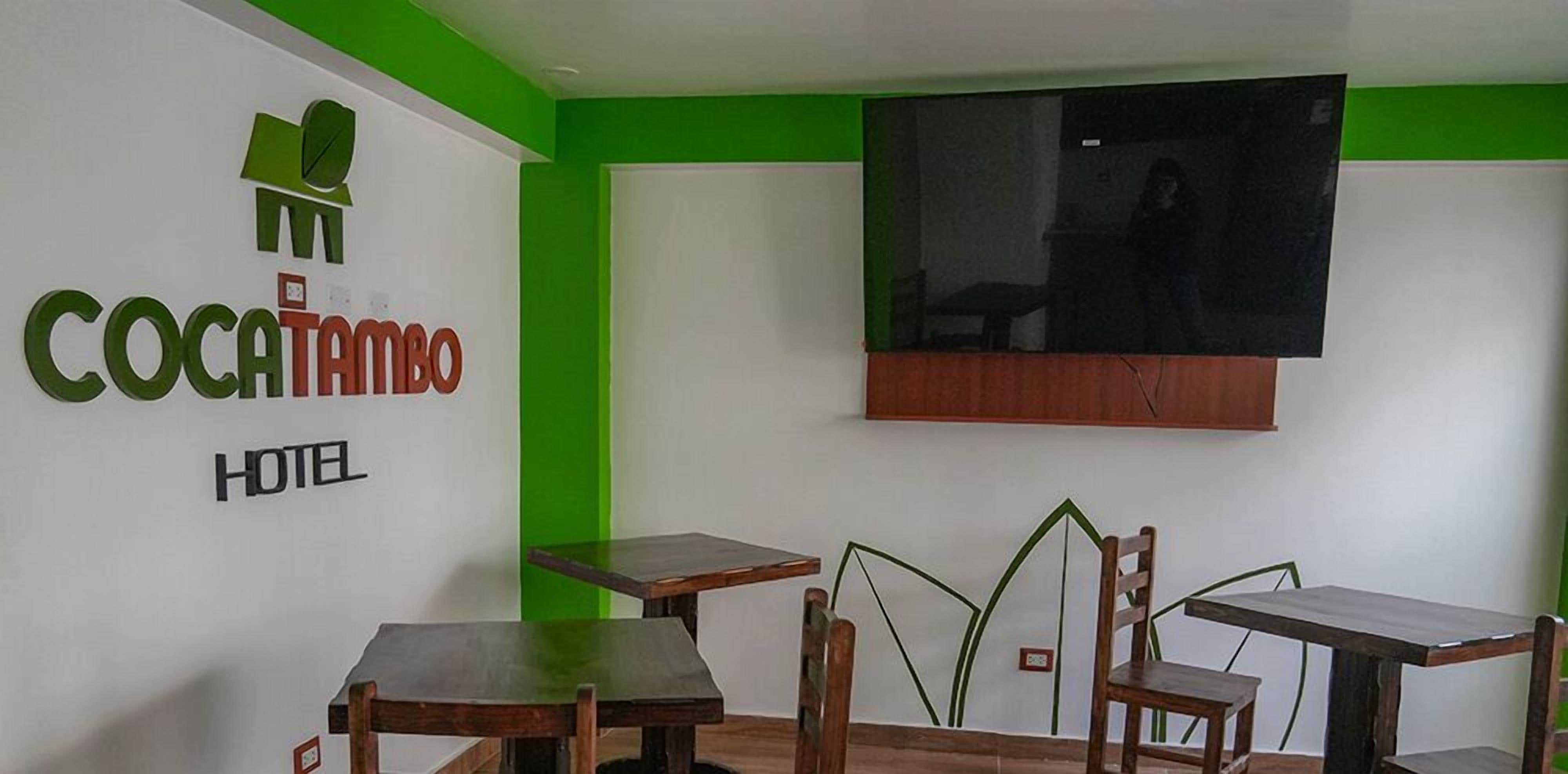 Habitación de hotel con pared verde decorativa, un televisor montado sobre una mesa de madera y un letrero que dice "Cocatambo Hotel".