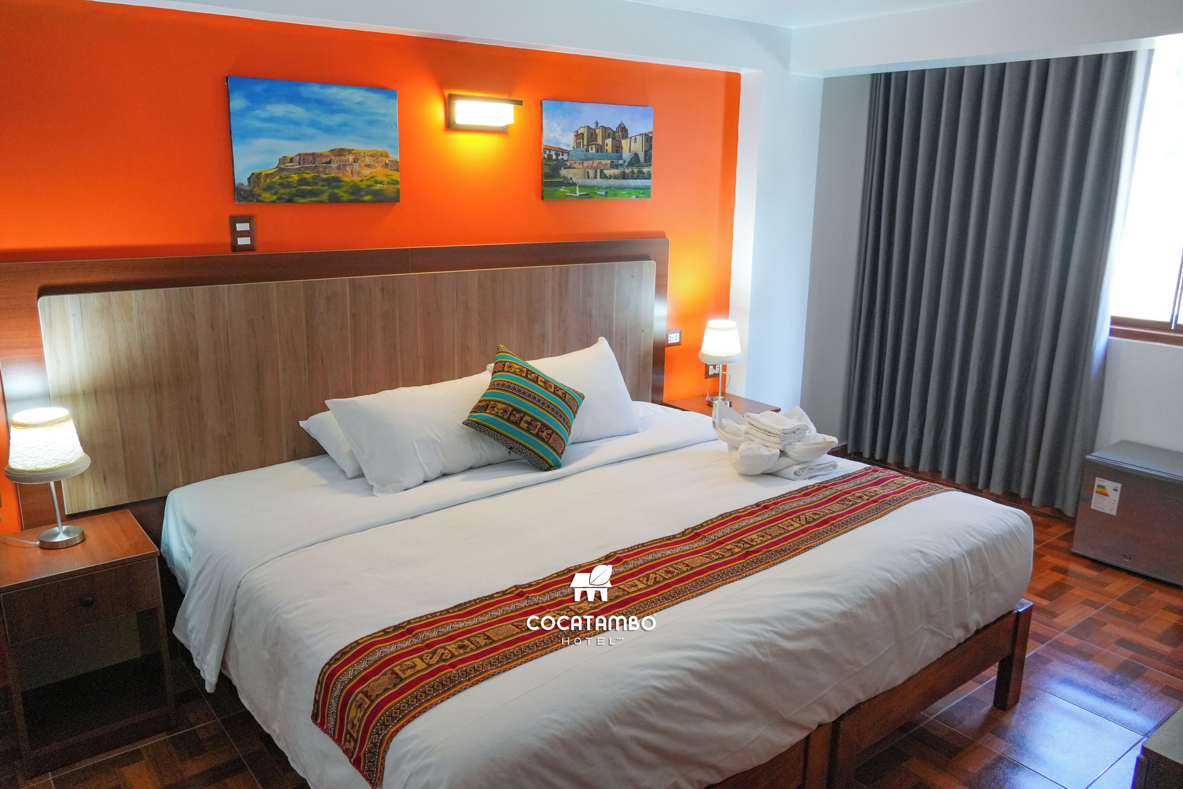 A hotel room with a large bed, two paintings on the wall, a wooden headboard, and a window with curtains.
