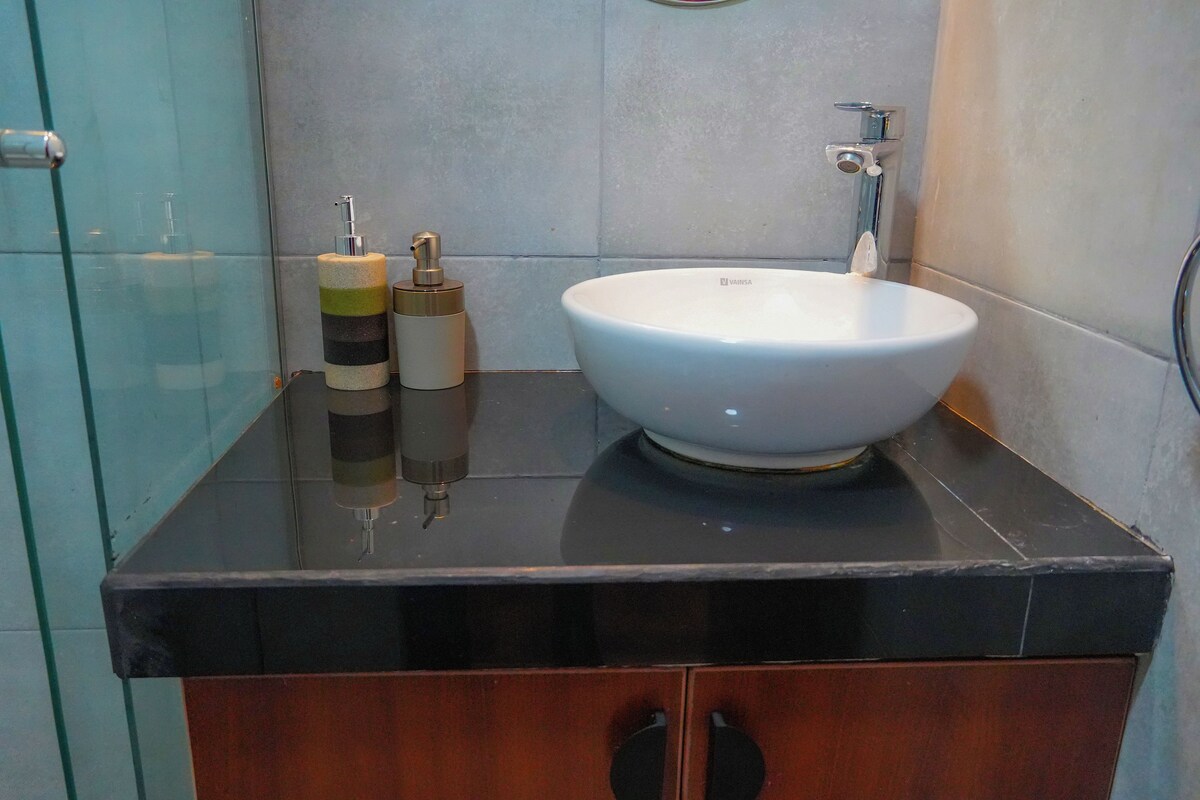 A bathroom with a white sink, a black countertop, and a wooden cabinet below.