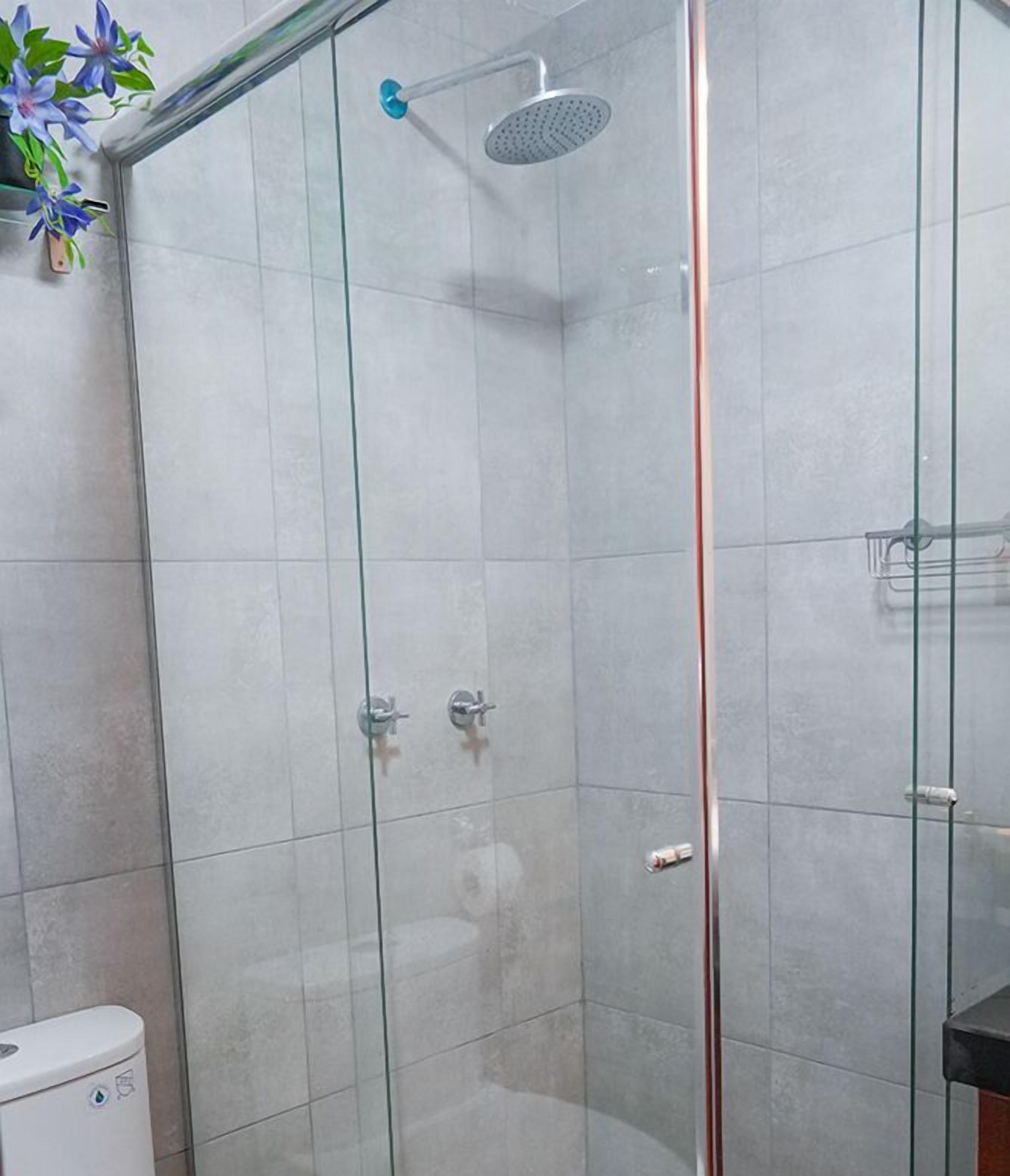 A glass-enclosed shower stall with a handheld showerhead and a wall-mounted control panel.