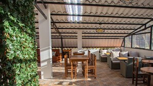 Un espace extérieur aménagé en terrasse, avec des tables et des chaises en bois, un coin salon abrité et une vue sur l’extérieur.