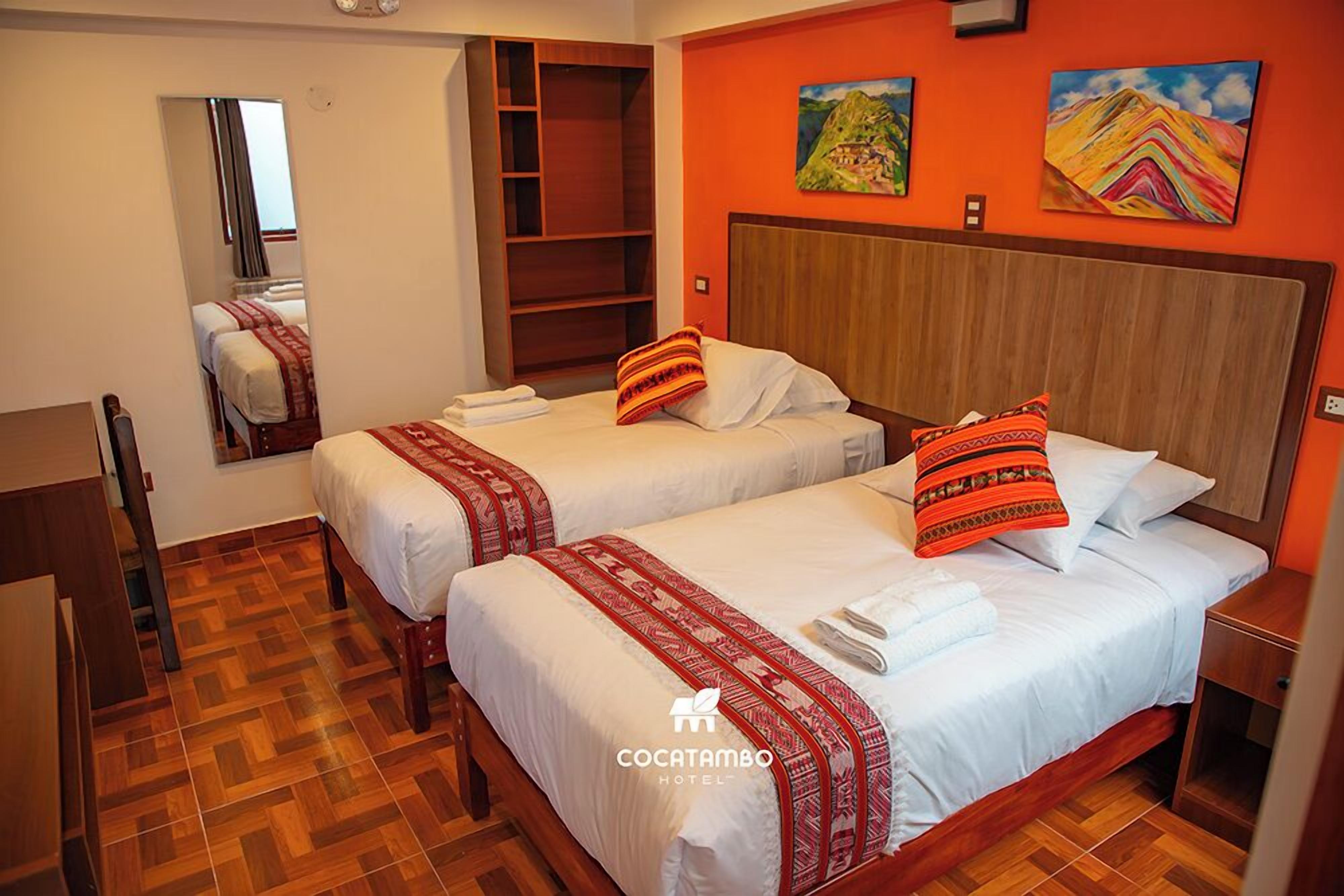 Habitación de hotel con dos camas, suelo de madera, un espejo grande y obras de arte en las paredes.