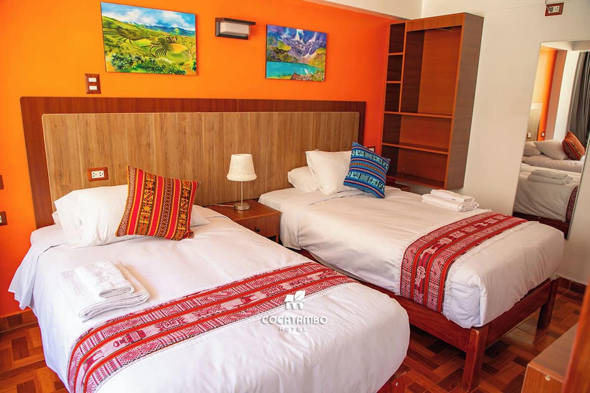 A hotel room with two beds, orange walls, and artwork.
