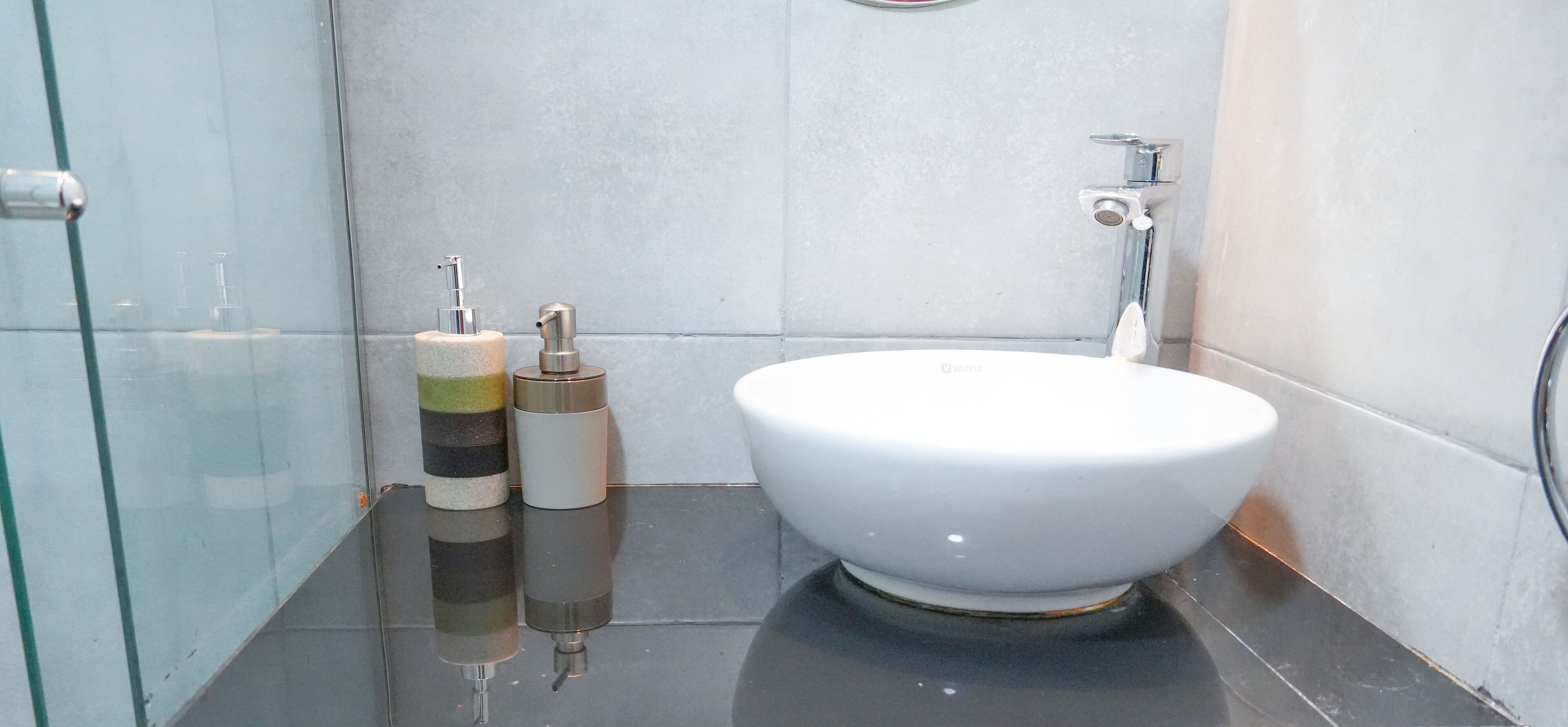 Ein modernes Badezimmer mit einem weißen Waschbecken, zwei Seifenspendern und einer Duschkabine aus Glas.