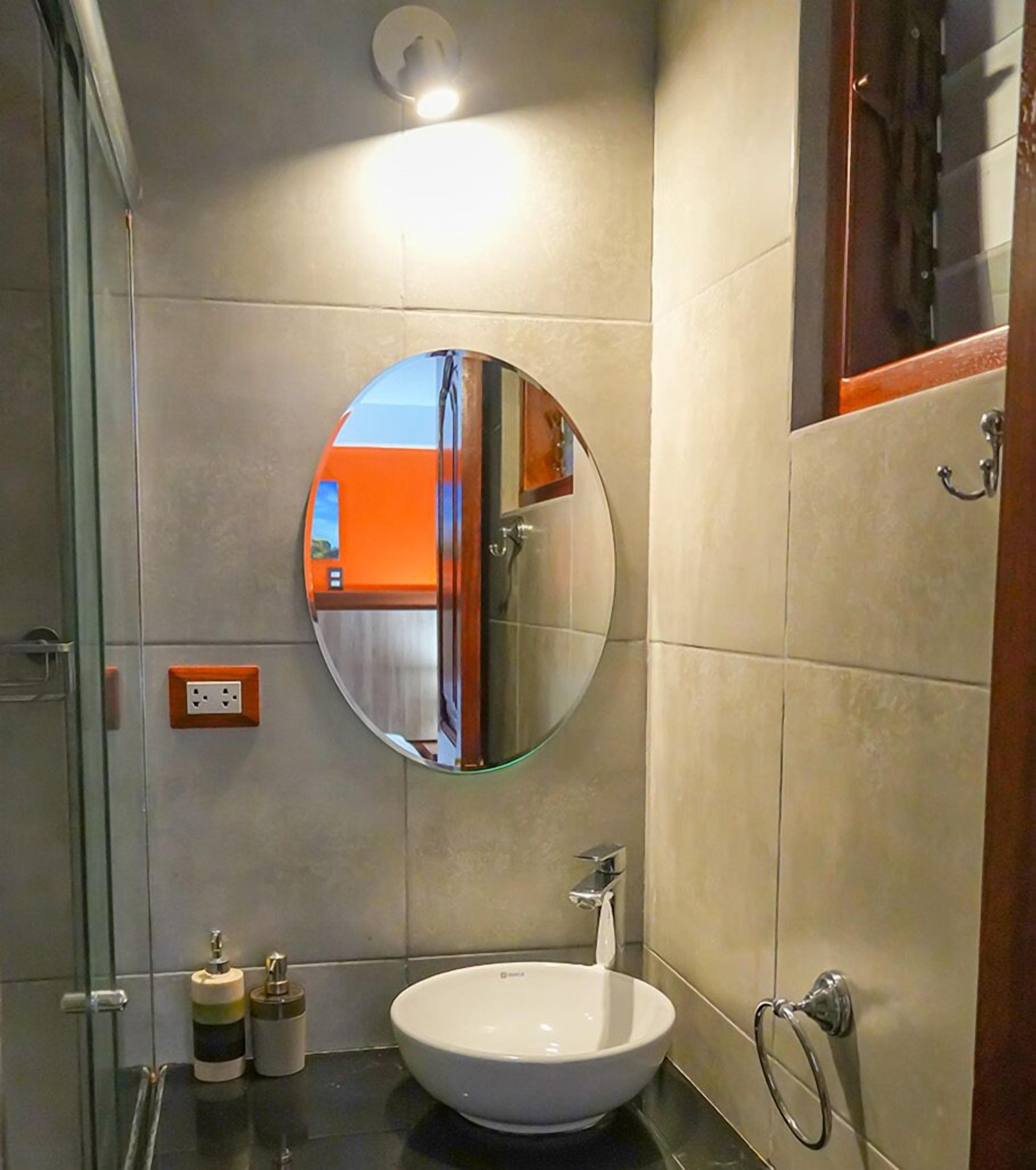 Casa de banho com espelho redondo, lavatório branco e cabine de duche em vidro.