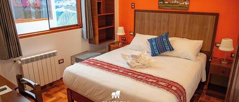 A hotel room with a wooden bed, a window with a view of mountains, a wooden nightstand, and a red wall.