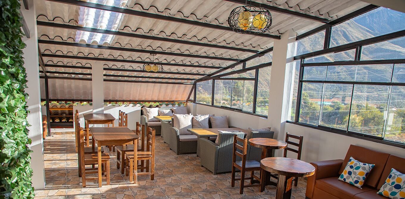 An outdoor patio with wooden furniture, a seating area, and large windows offering a view of the surrounding landscape.