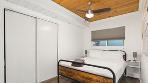 A bedroom with a wooden bed frame, white bedding, a ceiling fan, a window with blinds, and a white wardrobe. - Midtown Reno 1br W/ share Hot Tub & Backyard (Reno)