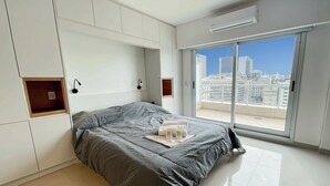 A modern bedroom with a large bed, built-in storage, a view of the city, and a sliding glass door to the balcony. - Studio Luxury Balcony Pool (Buenos Aires)