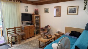 A cozy room with a bed, a TV, a wooden cabinet, a chair, and a fan.
