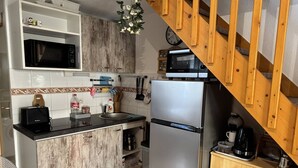 A compact kitchen with a microwave, toaster, sink, and stainless steel refrigerator. A wooden staircase leads to a loft area.