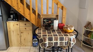 A kitchen with a wooden staircase, a table with a patterned tablecloth, a coffee maker, a basket, and a water dispenser.