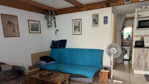 A cozy living room with a blue sofa, a wooden coffee table, and a patterned rug. There is a kitchen area visible in the background.