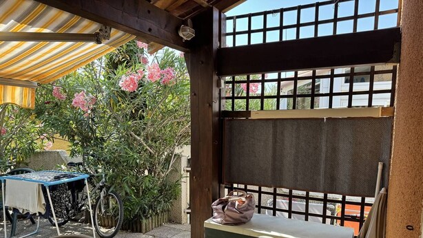 A covered outdoor seating area with a table and chairs, a bicycle, and a potted plant.