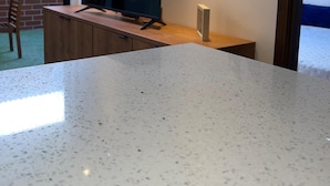 A modern kitchen with a granite countertop, a built-in TV, and a brick wall.