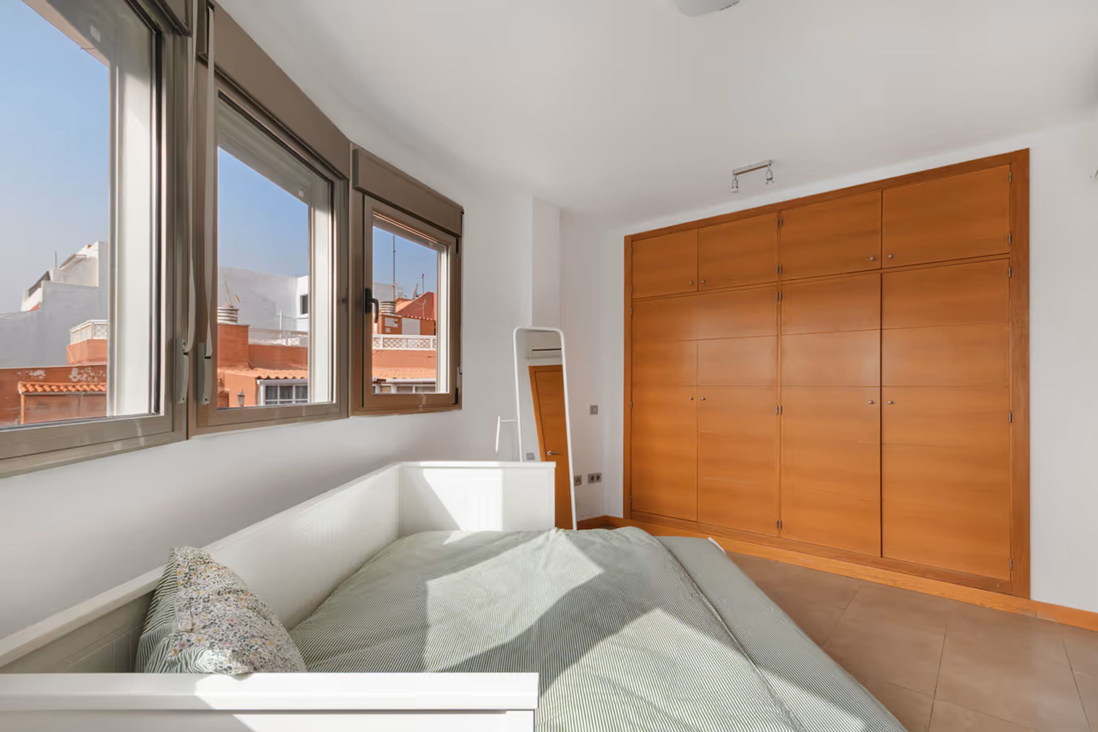Een slaapkamer met een bed, een houten garderobe en een raam met uitzicht op gebouwen.