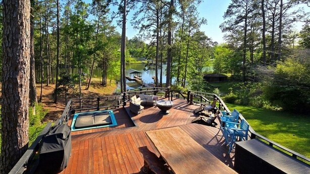 Une terrasse en bois, meublée pour l’extérieur, avec un foyer et une vue sur un lac entouré d’arbres.