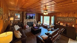 L’intérieur chaleureux d’un chalet avec une cheminée en pierre, un plafond en bois et un téléviseur.