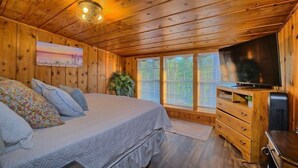 Une chambre dans un chalet en bois, avec un lit, une commode, une télévision et un tableau accroché au mur.