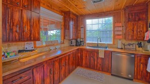 Une cuisine de style rustique, avec des meubles en bois, un lave-vaisselle en acier inoxydable et une fenêtre équipée de stores.