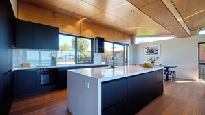 Une cuisine moderne dotée d’un grand îlot central, de meubles de rangement aux couleurs sombres et d’un revêtement de sol en bois.