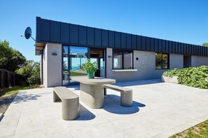 Un edificio moderno con tetto piatto, ampie finestre e un patio con tavolo e panche in cemento.