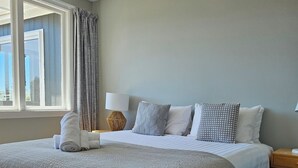 A neatly arranged bedroom with a large bed, a bedside table with a lamp, and a bench with a fluffy cover. - Close To Beach | Sunny | Getaway - KK16786 (Kaikoura)