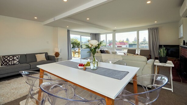 A modern living room with a dining area, large windows, and a view of the outside. - Close To Beach | Sunny | Getaway - KK16786 (Kaikoura)
