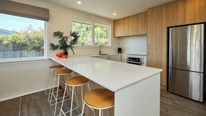 A modern kitchen with a large island, bar stools, a stainless steel refrigerator, and wooden cabinets. - Close To Beach | Sunny | Getaway - KK16786 (Kaikoura)