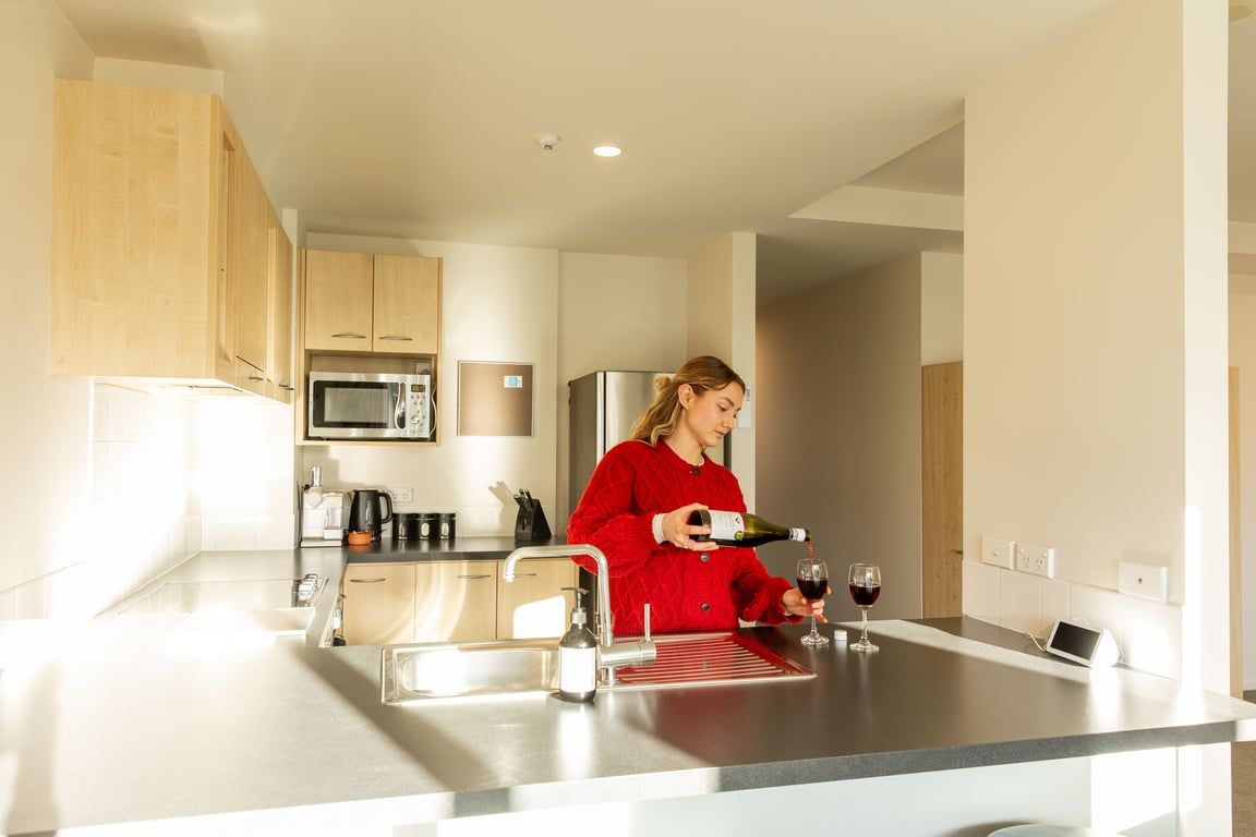 Une cuisine moderne équipée d’appareils électroménagers en acier inoxydable, d’un four à micro-ondes encastré, et une bouteille de vin dont on verse le contenu dans un verre.