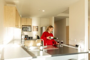 A modern kitchen with stainless steel appliances, a built-in microwave, and a wine bottle being poured into a glass.