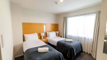 Een hotelkamer met twee bedden, een houten hoofdbord, bedlampen en een groot raam met gordijnen.