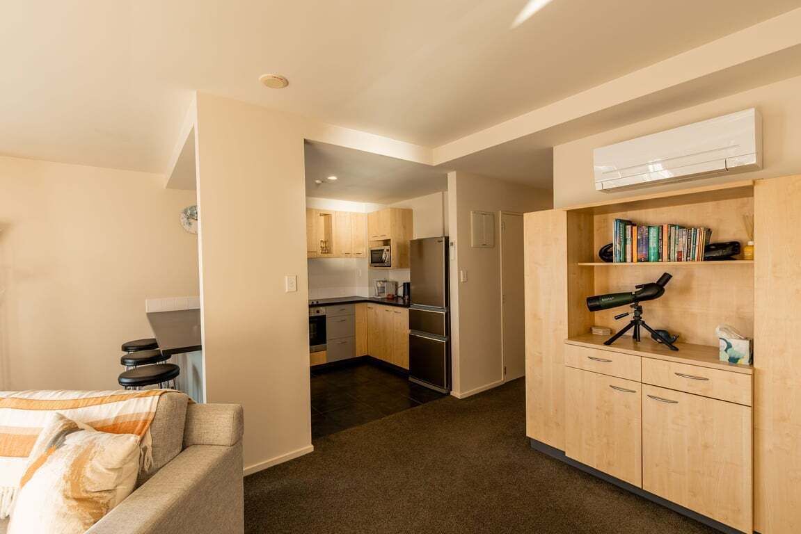 Een knus woongedeelte met een kitchenette, een bank, een boekenkast met boeken en een telescoop, en een kleine eethoek.
