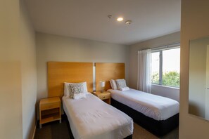 Habitación de hotel con dos camas individuales, cabecero de madera, mesita de noche y ventana con cortinas.