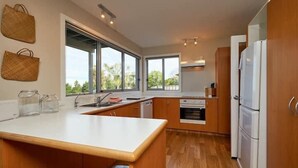A modern kitchen with wooden cabinets, a white countertop, and a large window providing natural light. - The Lookout | Spacious | Stunning Views - KK12632 (Kaikoura)