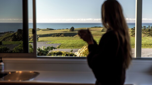 A person standing by a window with a view of a coastal landscape. - The Lookout | Spacious | Stunning Views - KK12632 (Kaikoura)