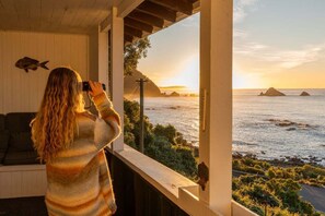 Eine Person fotografiert Meerblick vom Balkon mit Holzgeländer und einer Couch.