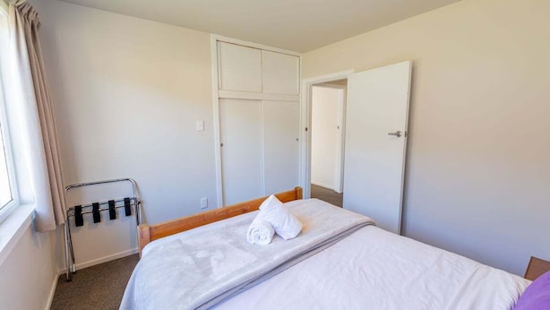 A hotel room with a bed, a wardrobe, a door, and a window with curtains.