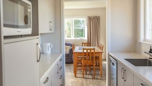 A compact kitchen with a microwave, a coffee maker, a dining table with chairs, and a window with curtains.