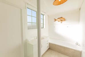 Un baño moderno con bañera, mampara de vidrio y un ventanal grande.