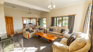 A spacious living room with a large wooden coffee table, two sofas, and a dining area visible through an open door. - Charming Villa | Family Friendly | Handy to Town - KK14769 (Kaikoura)
