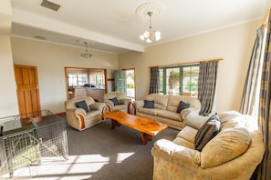 A spacious living room with a large wooden coffee table, two sofas, and a dining area visible through an open door. - Charming Villa | Family Friendly | Handy to Town - KK14769 (Kaikoura)