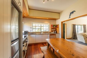 A kitchen with wooden cabinets, a stainless steel refrigerator, a wooden dining table, and a window with curtains. - Charming Villa | Family Friendly | Handy to Town - KK14769 (Kaikoura)