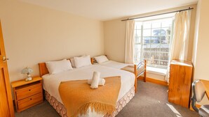 A hotel room with a large bed, a bedside table, a chair, and a window with curtains. - Charming Villa | Family Friendly | Handy to Town - KK14769 (Kaikoura)