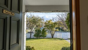 A view from a doorway to a lawn with a white fence and trees, and a mountain in the background. - Charming Villa | Family Friendly | Handy to Town - KK14769 (Kaikoura)