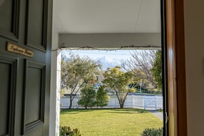 A view from a doorway to a lawn with a white fence and trees, and a mountain in the background. - Charming Villa | Family Friendly | Handy to Town - KK14769 (Kaikoura)