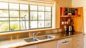A kitchen with a large window, stainless steel sink, wooden cabinets, and a kettle on the counter. - Charming Villa | Family Friendly | Handy to Town - KK14769 (Kaikoura)