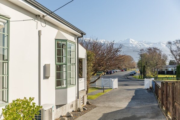 A residential street with a white house, a clear sky, and a mountain range in the background.